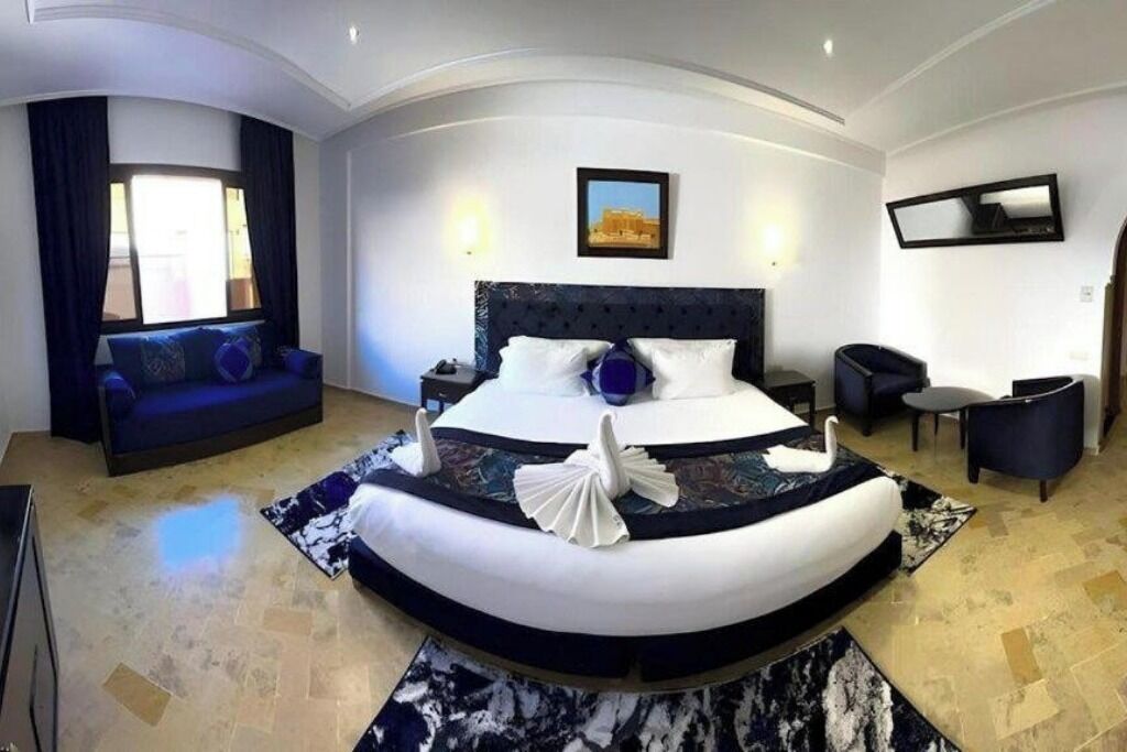 A modern hotel room with a curved bed, a sofa, a small table, and a wall-mounted TV.