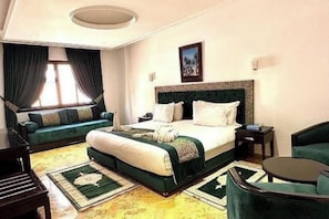 A hotel room with a large bed, a sofa, a small table, and a piano. - Riad Dar Chafik (Marrakech)