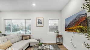 A modern living room with a sectional sofa, a glass coffee table, and a large landscape painting on the wall.