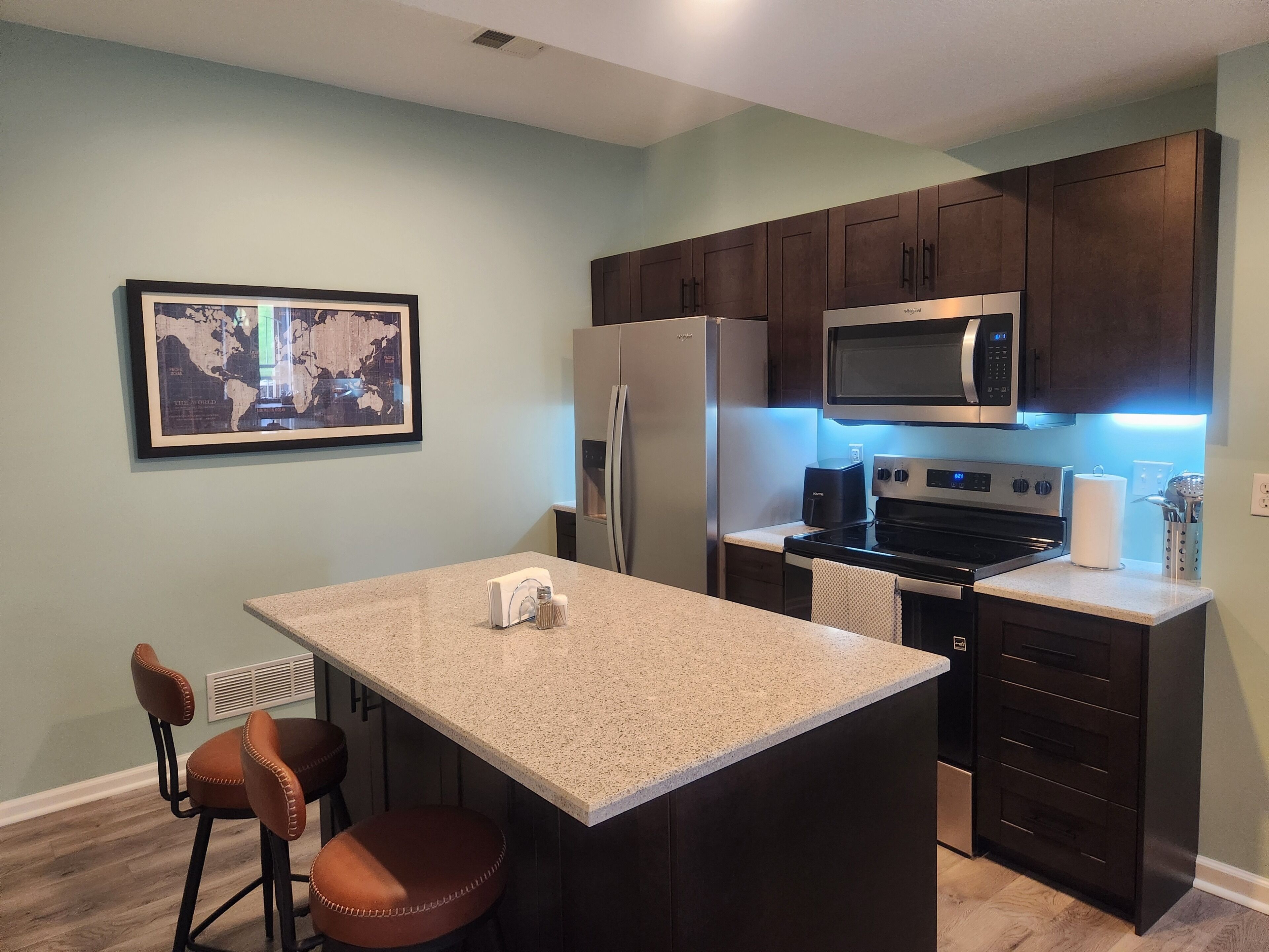 A kitchen with dark wooden cabinets, a stainless steel refrigerator, a microwave, and a granite countertop.