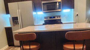 Una cocina con armarios de madera oscura, un refrigerador blanco, un microondas, una estufa y dos taburetes de bar.
