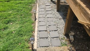 Un sendero de piedra que lleva a una terraza de madera, rodeada de un césped cuidado.
