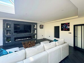 A modern living room with a large flat-screen TV, a white leather sofa, and a stone accent wall. - 4 Bedroom Luxury Home Features Hottub & Pool Table (Northwood)