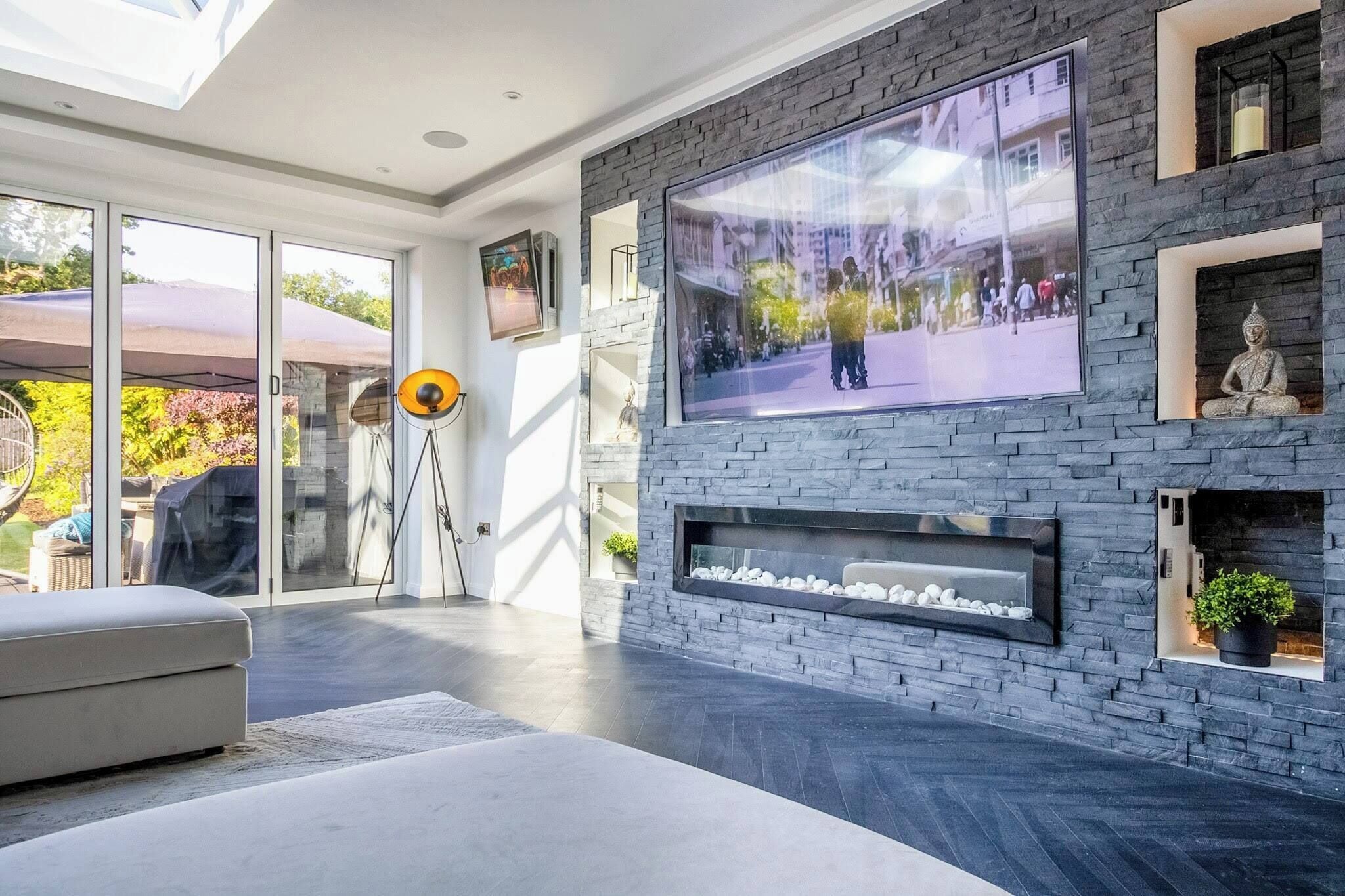 A modern living room with a large flat-screen TV mounted on a stone wall, a fireplace below, and a comfortable seating area with a sofa.