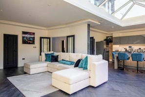 A modern living room with a sectional sofa, a dining area with bar stools, and a kitchen in the background. - 4 Bedroom Luxury Home Features Hottub & Pool Table (Northwood)