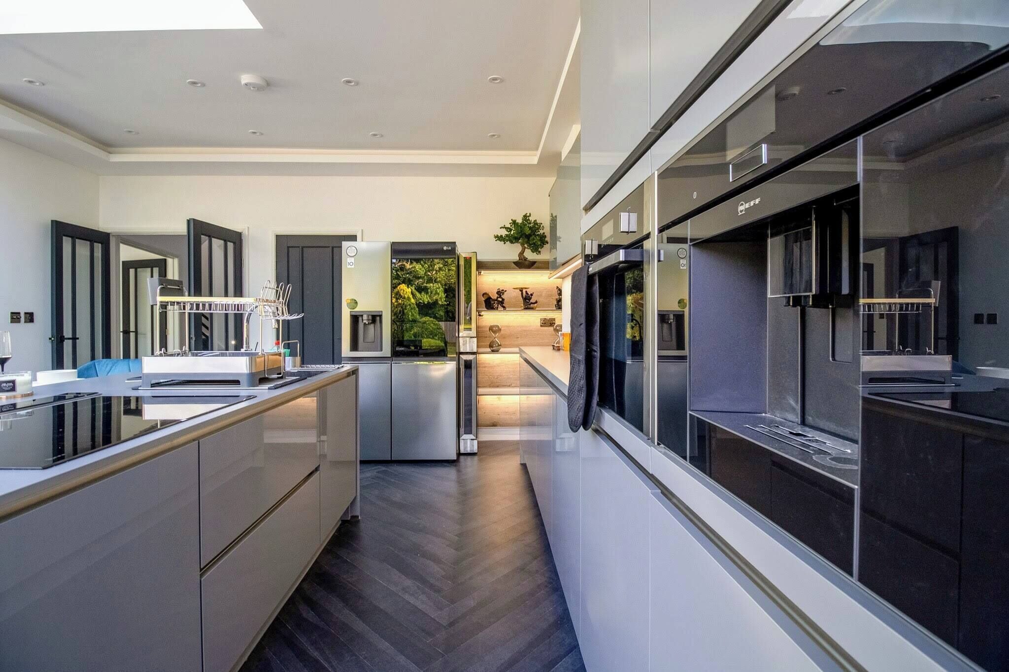 Een moderne keuken met een centraal eiland, geïntegreerde apparatuur en uitzicht op een tuin.