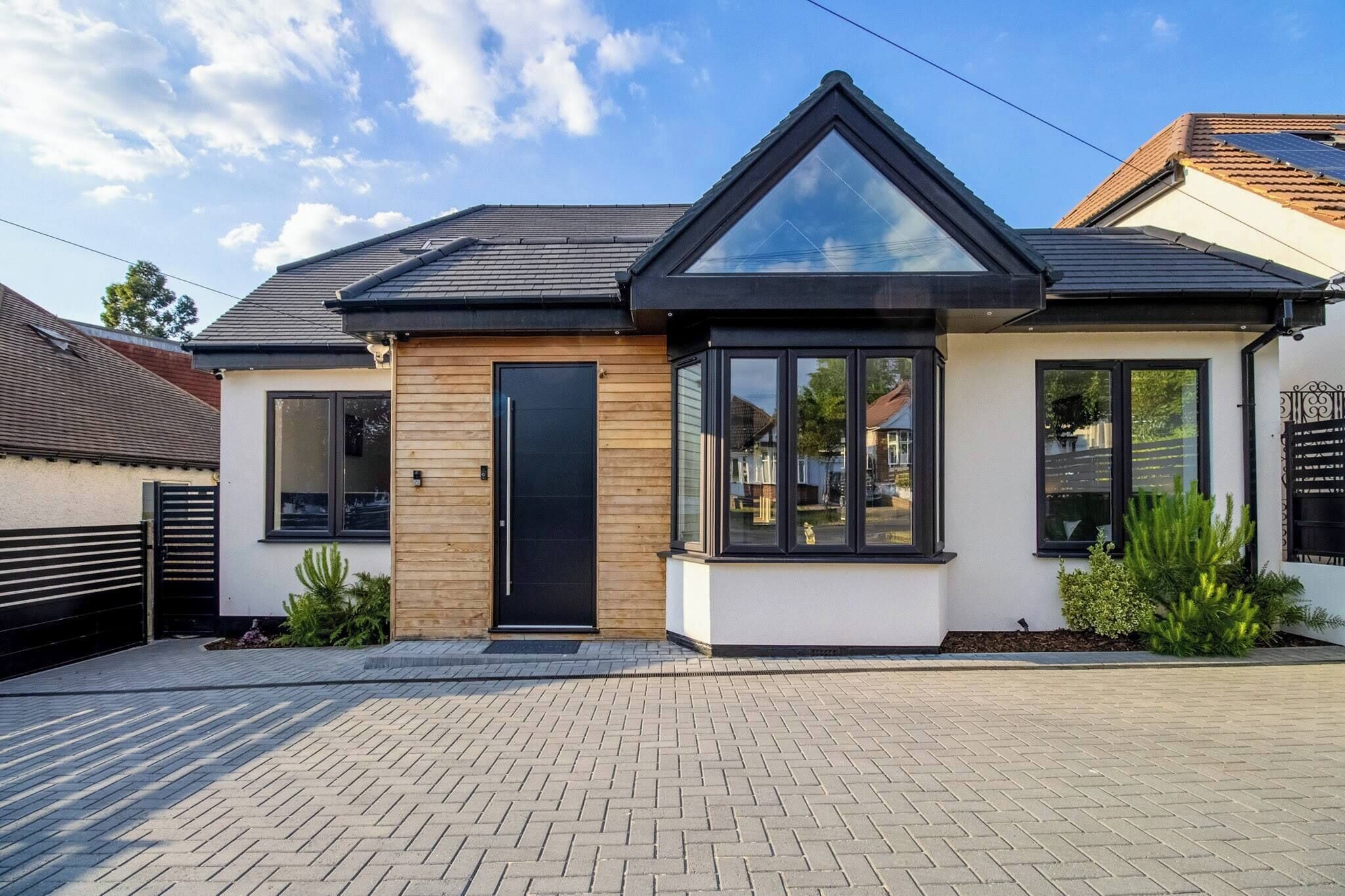 A modern two-story house with a black roof, large windows, and a wooden door.