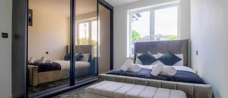 A bedroom with a large bed, a sliding glass door leading to a balcony, and a window providing natural light.