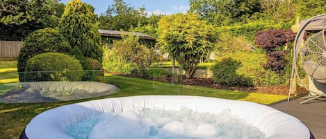 An outdoor hot tub surrounded by a well-maintained garden with various shrubs and trees.