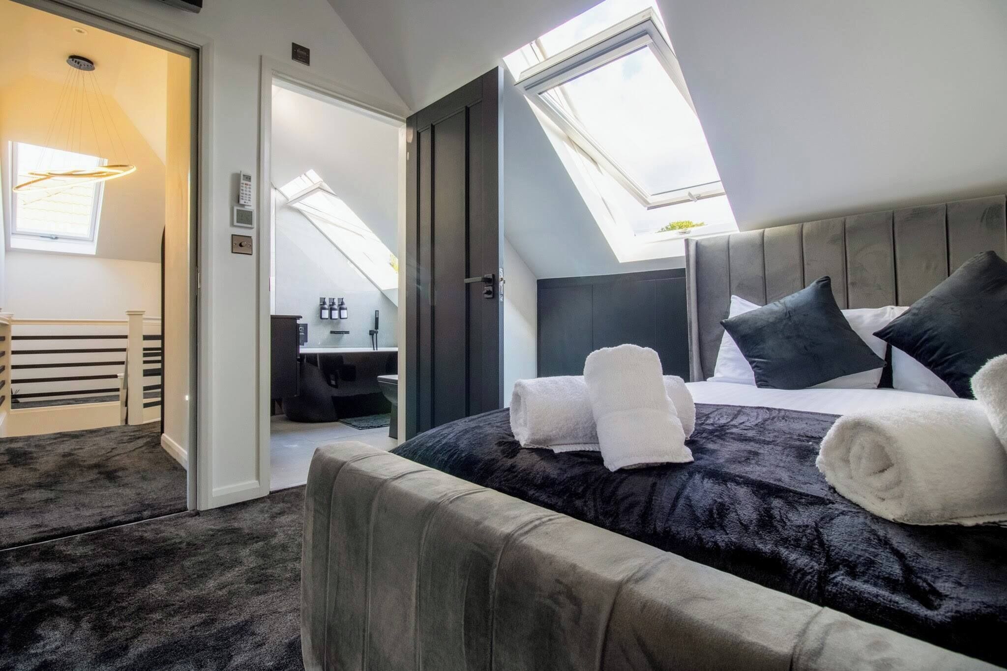 A modern hotel room with a large bed, a skylight, a bathroom, and a seating area.