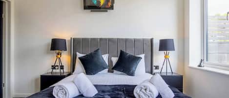 A neatly made bed with a grey headboard, two bedside lamps, and a painting above the bed.