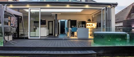 A modern house with a covered patio, a hot tub, and a glass-enclosed living area.