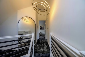 A staircase with a black and white striped railing, a black carpeted floor, and a modern light fixture with concentric circles. - 4 Bedroom Luxury Home Features Hottub & Pool Table (Northwood)