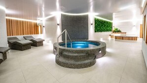 Ein moderner Wellnessbereich mit einer zentralen Whirlwanne, Sitzbereichen und einer Rezeption.