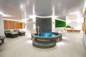 Un moderno espacio interior de spa con una bañera de hidromasaje central, zonas de estar y un mostrador de recepción.