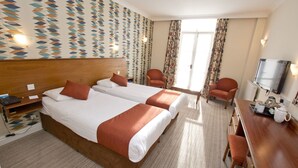Ein Hotelzimmer mit zwei Betten, einem Schreibtisch mit Fernseher und einem Sessel.