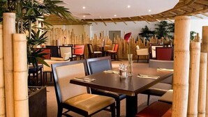 Ein Restaurant mit Bambusstützen, gepolsterten Stühlen und einem zentralen Esstisch.