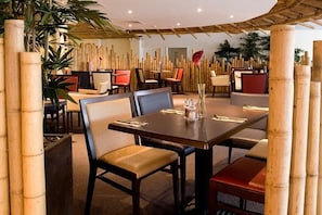 Ein Restaurant mit Bambusstützen, gepolsterten Stühlen und einem zentralen Esstisch.