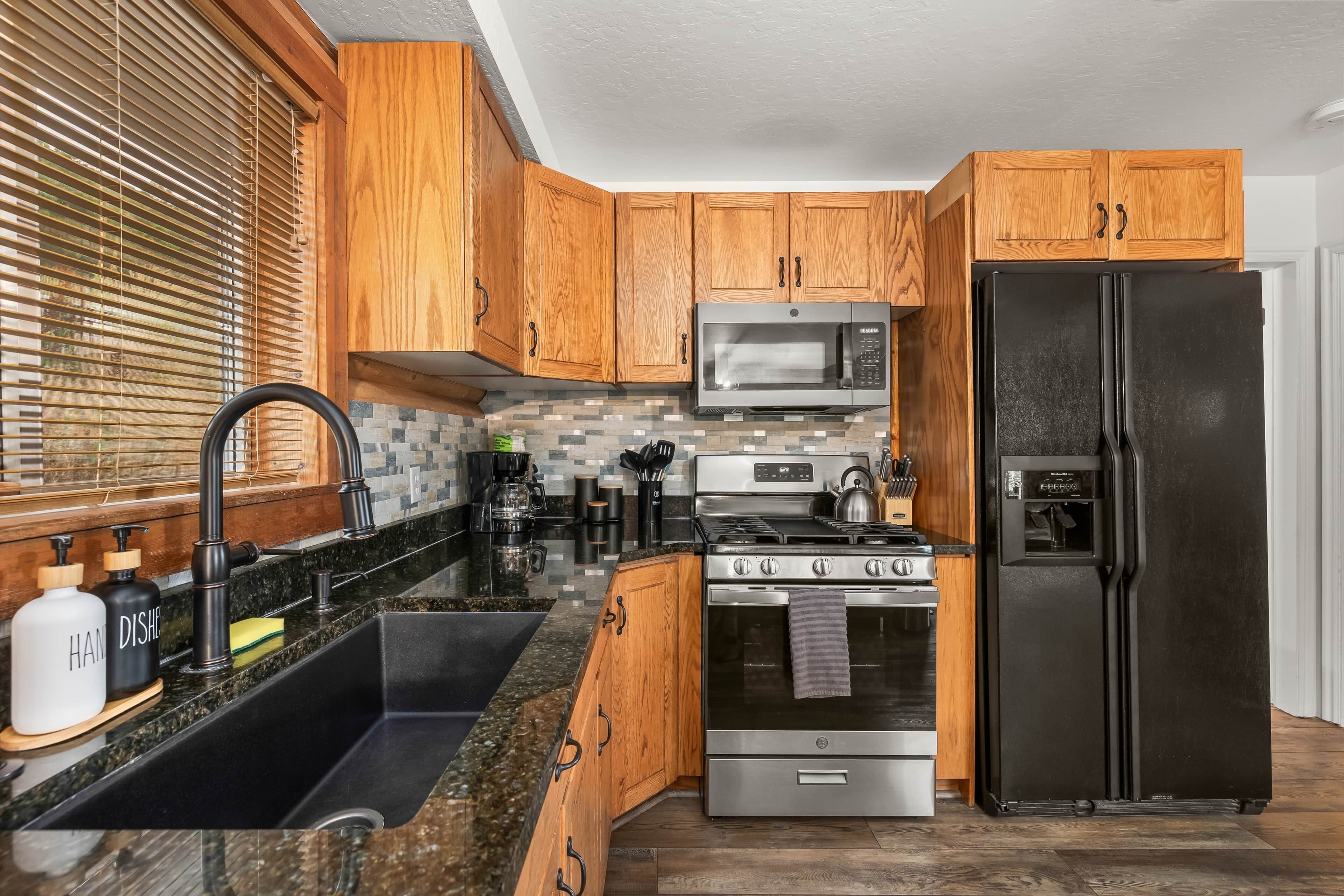 A kitchen with wooden cabinets, a stainless steel refrigerator, a microwave, a stove, and a sink.