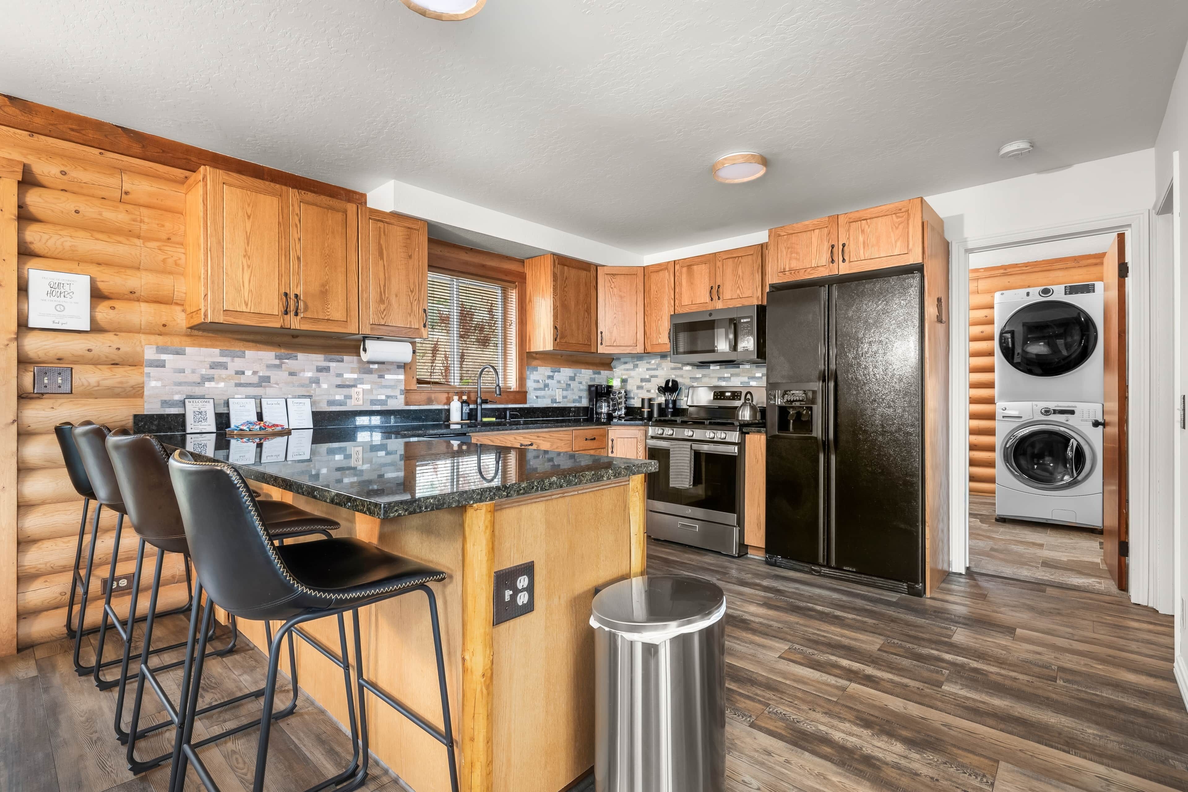 A modern kitchen with wooden cabinets, a central island with bar stools, stainless steel appliances, and a built-in washer and dryer.