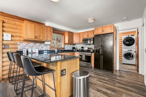 A modern kitchen with wooden cabinets, a central island with bar stools, stainless steel appliances, and a built-in washer and dryer.