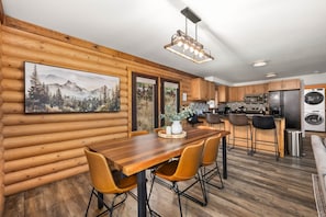 A log cabin interior with a dining area, kitchen, and a large window with a mountain view. - Midway Mountain Cabin (Wasatch County)