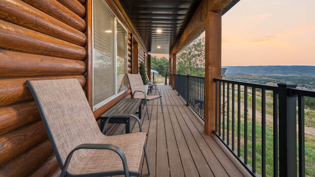 Terraza de madera con dos sillas de descanso y una mesa, con vistas a un paisaje pintoresco.