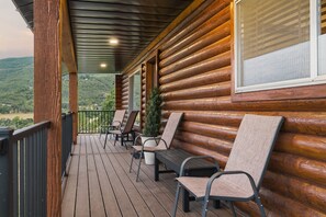 En timmerstuga med en träveranda, utomhusmöbler och utsikt över bergen.