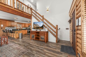 A spacious living area with a wooden staircase, a kitchen with bar stools, and a mounted television.