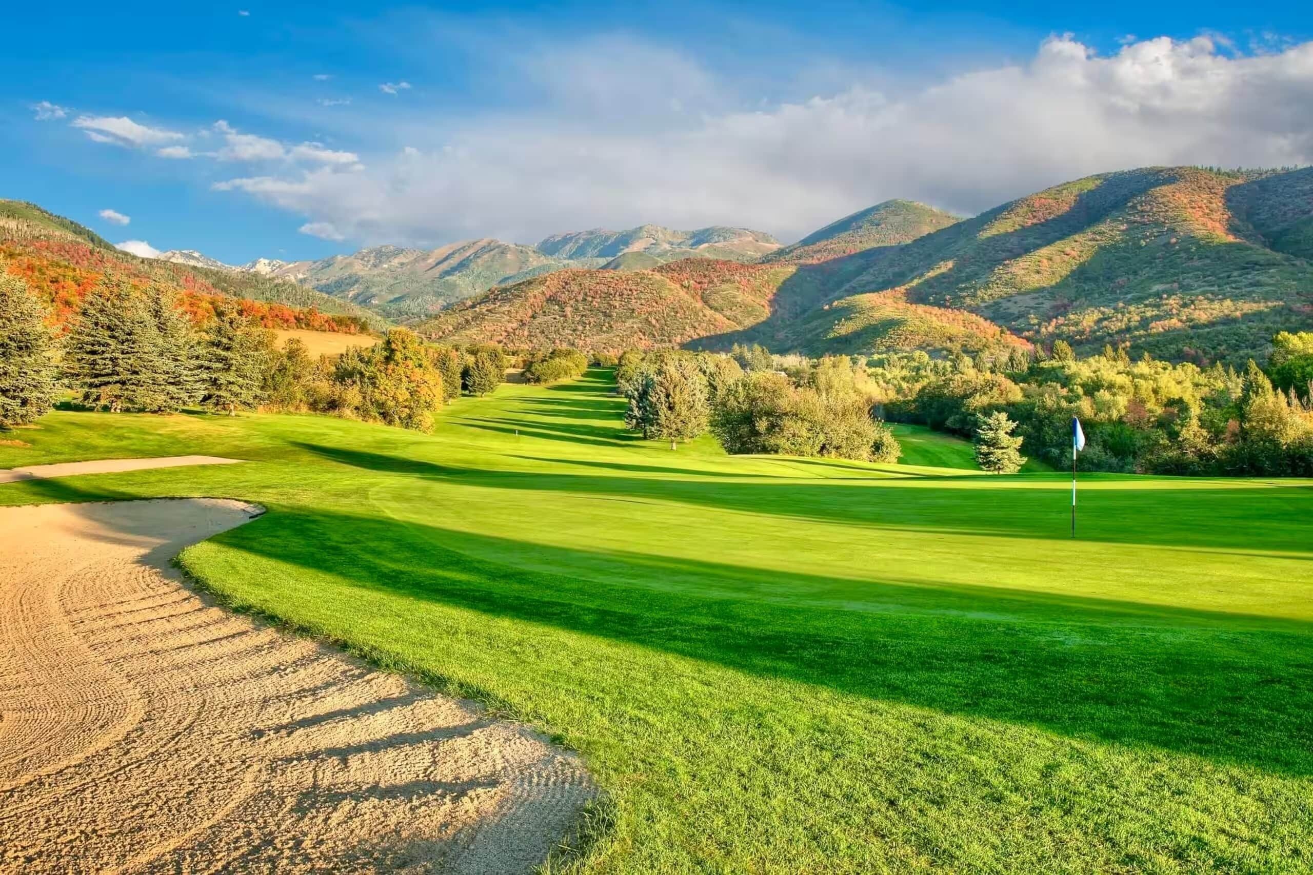 Un parcours de golf avec un chemin bien défini menant au trou, entouré d’une végétation luxuriante et avec des montagnes en arrière-plan.