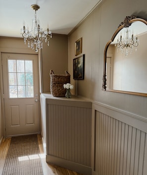 A hallway with a wooden door, a wicker basket, a framed picture, and a mirror.