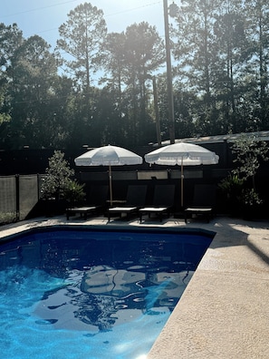A swimming pool with lounge chairs and umbrellas, surrounded by trees.