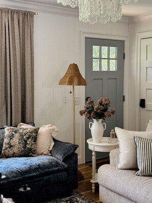 A room with a dark blue sofa, a white armchair, a floor lamp, and a vase of flowers on a small table.