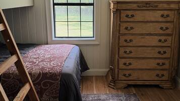 Un dormitorio con literas, cómoda, ventana con vistas a la vegetación y un candelabro.