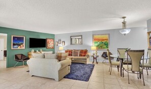 A living room with a sofa, a coffee table, and a dining area with chairs and a table. - Phoenix Towers - Charming Condo, Private Ocean Access - Singer Island - 2BR, 2BA (Riviera Beach)