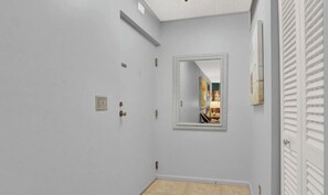A hallway with a door, a light switch, and a mirror on the wall. - Phoenix Towers - Charming Condo, Private Ocean Access - Singer Island - 2BR, 2BA (Riviera Beach)