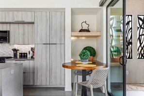 A modern kitchen with a built-in oven, a dining area with a round table, and a potted plant. - Daybreak | custom pool, spa, sauna, wellness room (Twentynine Palms)