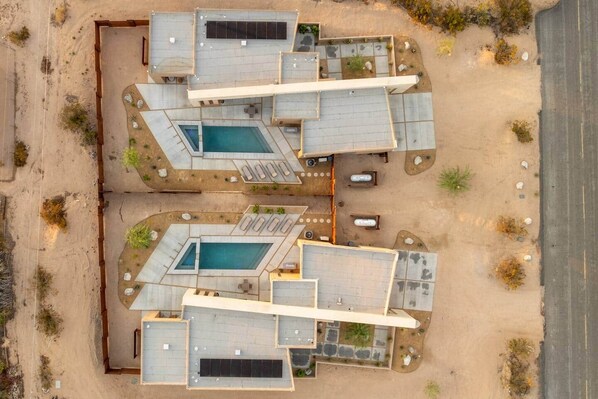 A modern hotel with multiple swimming pools, outdoor seating areas, and a desert landscape.