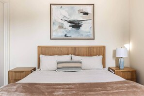 A neatly made bed with a wooden headboard, two bedside tables, and a wall-mounted abstract painting.