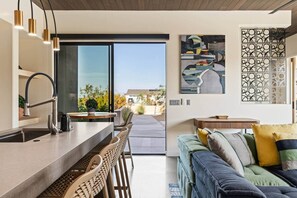 A modern kitchen with a dining area, a sofa, and a view of the outdoors.