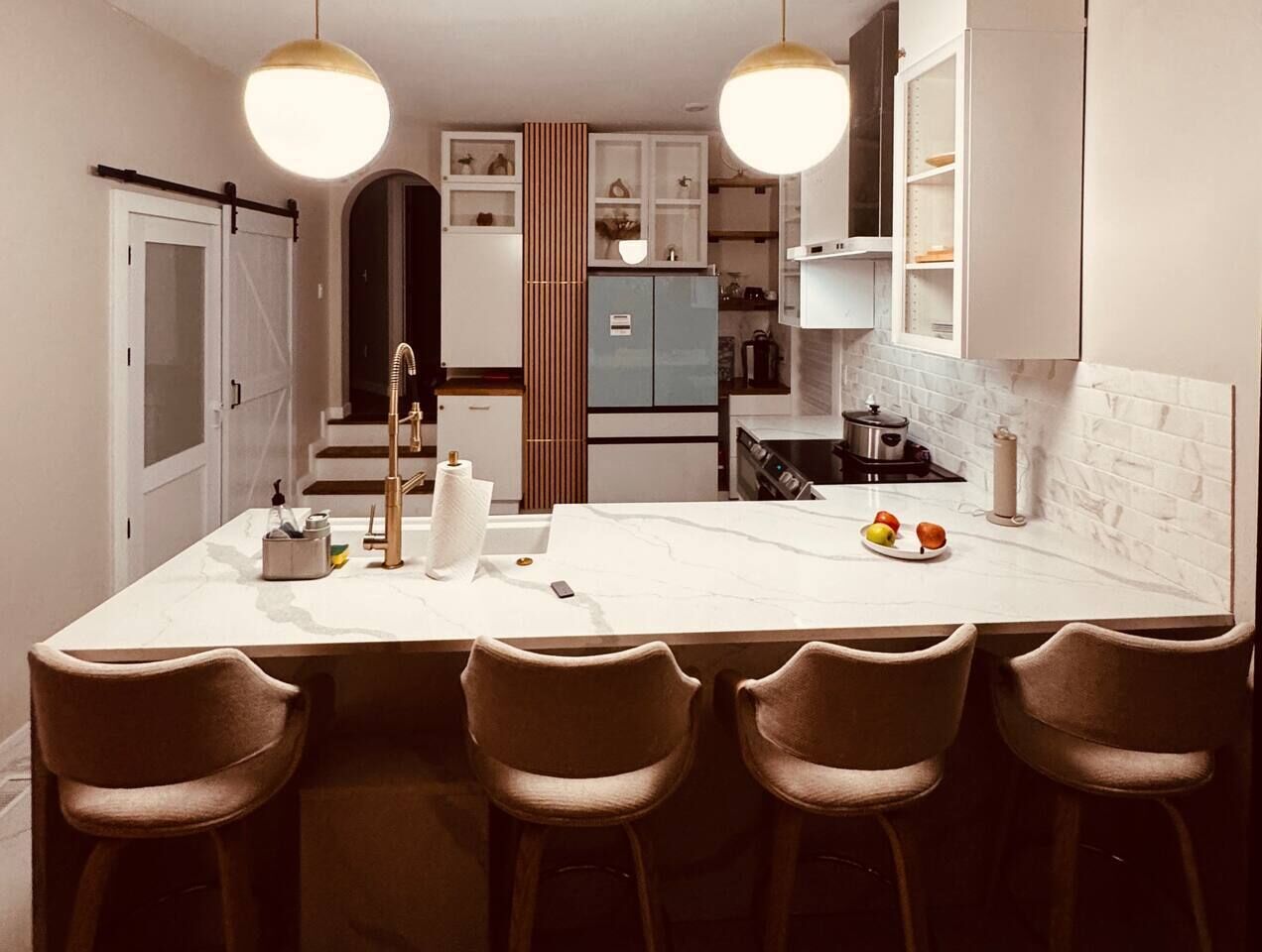 Une cuisine moderne dotée d’un plan de travail en marbre, d’un îlot central avec des tabourets de bar et d’appareils électroménagers intégrés.