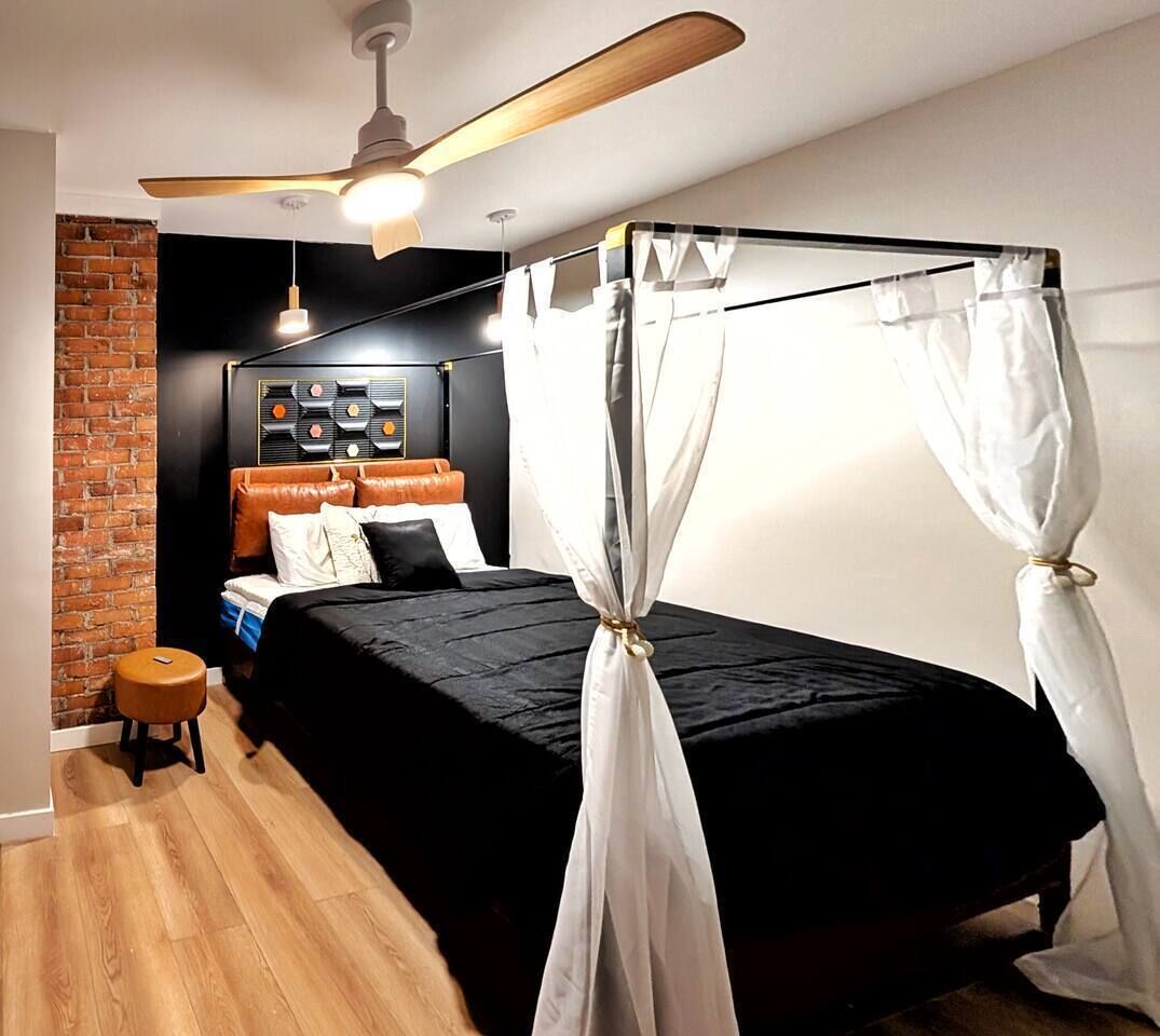 Une chambre à coucher avec un lit à baldaquin, un ventilateur de plafond, un mur en briques et un petit tabouret.