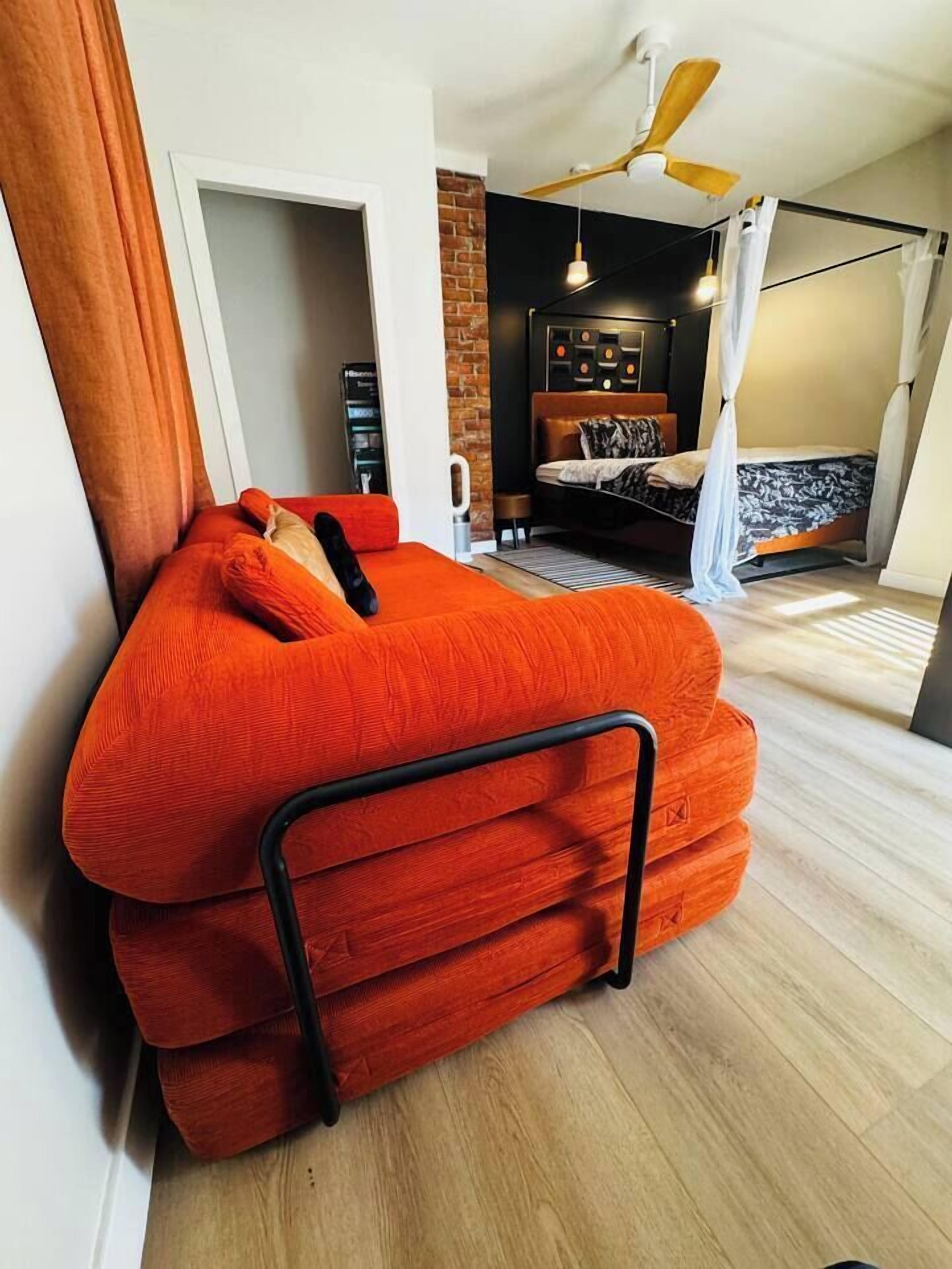 A room with a large orange sofa, a ceiling fan, and a bed with a canopy.