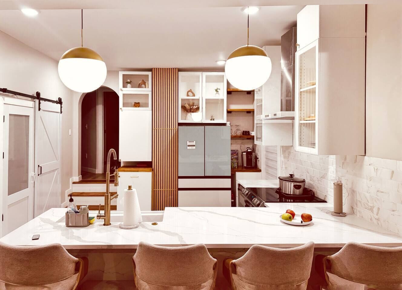 A modern kitchen with a central island, pendant lighting, and a dining area with chairs.