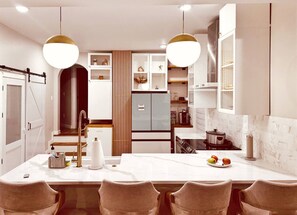 A modern kitchen with a central island, pendant lighting, and a dining area with chairs.