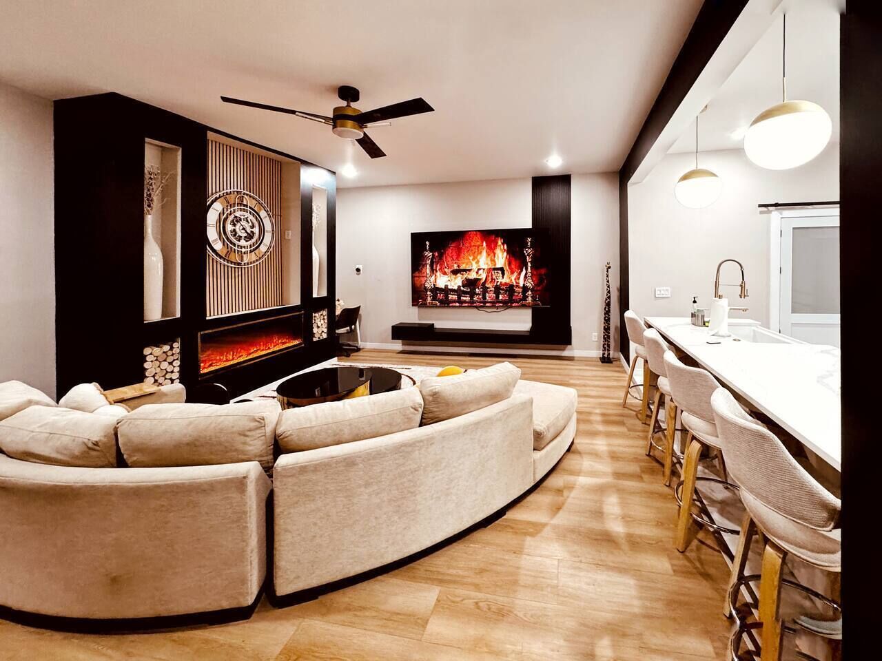 A modern living room with a sectional sofa, a fireplace, a television, and a dining area with bar stools.