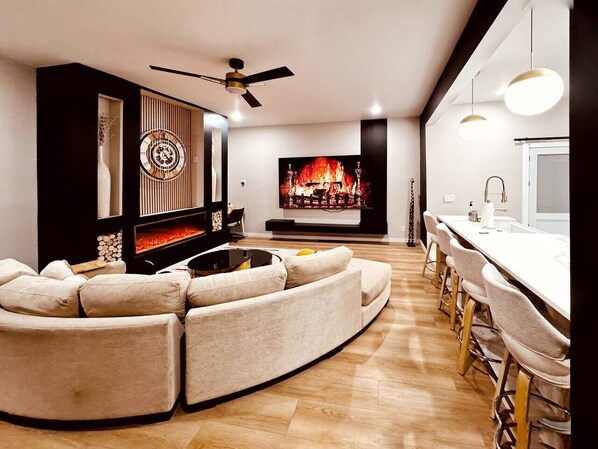 A modern living room with a sectional sofa, a fireplace, a television, and a dining area with bar stools.