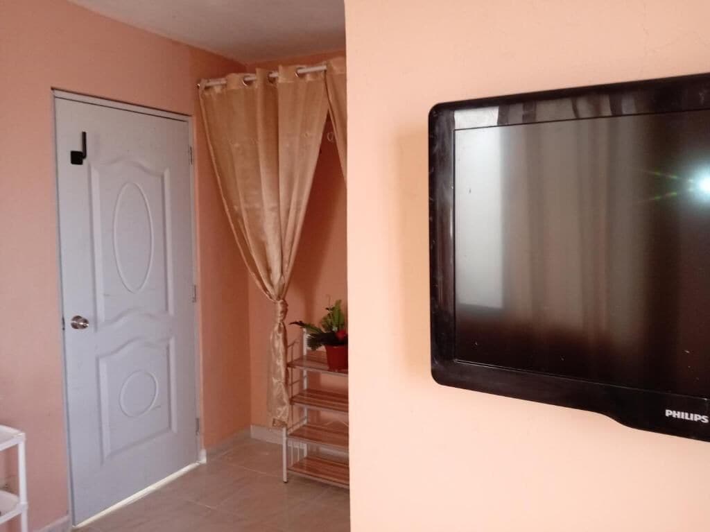 A room with a closed door, a curtain, a staircase, and a mounted television.