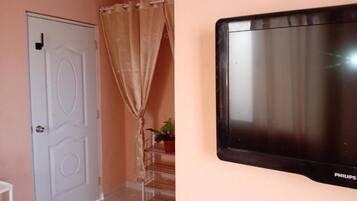 A room with a closed door, a curtain, a staircase, and a mounted television.