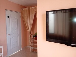A room with a closed door, a curtain, a staircase, and a mounted television.